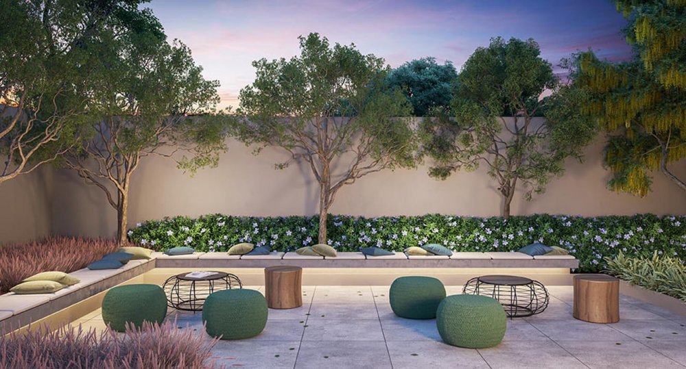 Praça de convivência com bancos, pufes e jardins floridos ao entardecer